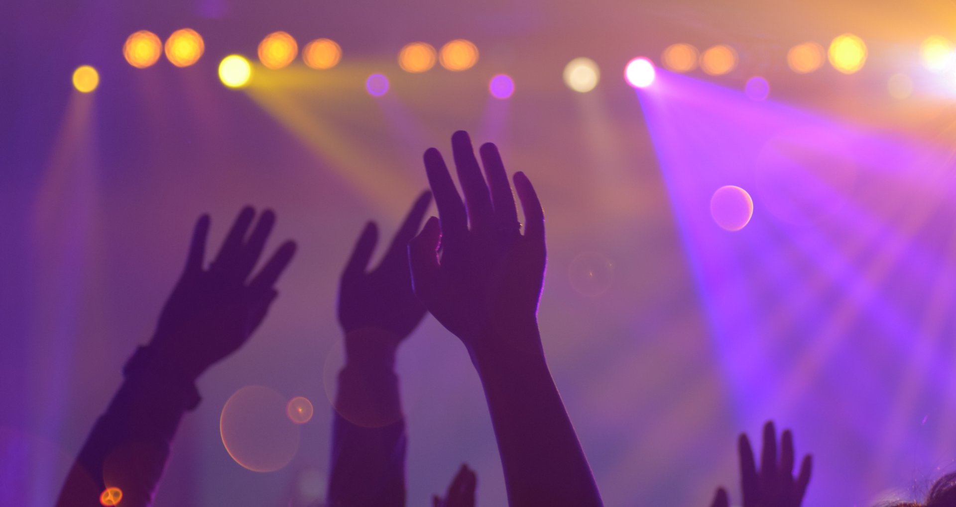 Publikum bei einem Konzert mit erhobenen Händen, warme Bühnenlichter
